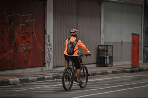 Cyclist in orange jacket commuting through a gritty urban street on a city bike, riding safely in a marked bike lane.