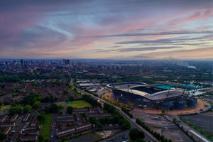 Aerial view of Manchester city skyline and Etihad Stadium at sunset.