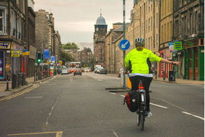 Cyclist in hi-vis jacket signalling a turn on a city street in the UK, riding safely through urban traffic vivup cycle to work