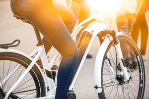 Close-up of a person on a white electric bike, with sunlight flaring in the background, showcasing the battery placement on the bike frame and casual riding attire