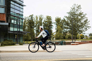 Woman commuting on a black electric bike past modern glass buildings in the city.