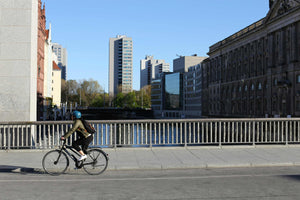 Cyclist commuting across city bridge with modern skyscrapers and historic buildings in the background.