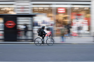 Cyclist on a commuter electric bike riding past a busy urban street, highlighting the speed and efficiency of e-bikes for city commuting.