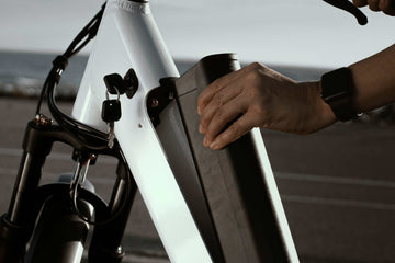 Close-up of a rider securing or removing the battery on an electric bike using a key lock system.