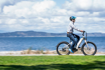 A man riding a modern electric bike along a coastal path with sea and hills in the background. Perfect example of affordable electric bikes under £1,500 in the UK.