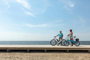 Two seniors enjoying a scenic ride on step-through electric bikes by the seaside – ideal e-bikes for elderly riders seeking comfort, stability, and ease of use in the UK.