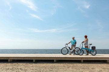 Two seniors enjoying a scenic ride on step-through electric bikes by the seaside – ideal e-bikes for elderly riders seeking comfort, stability, and ease of use in the UK.