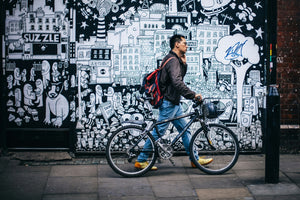 Man walking with an urban electric bike in front of vibrant street art, capturing the blend of modern commuting and city culture.