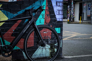 Close-up of a Falcon electric bike against a graffiti wall, showcasing its sleek black frame and urban commuter design.