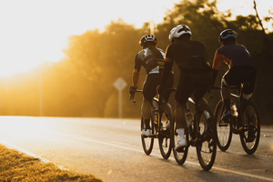 Three cyclists riding in a group on a road during sunset, with golden light illuminating their figures and casting long shadows, capturing a peaceful evening ride.