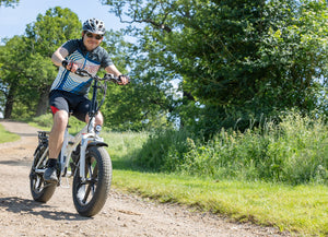 A rider enjoying an outdoor adventure on a white Hygge Vester Step electric bike with fat tyres, a foldable frame, and a powerful 250W motor. Designed for both off-road trails and urban commuting, this e-bike offers an 80km range for long-distance rides. Available at Glide & Gear.