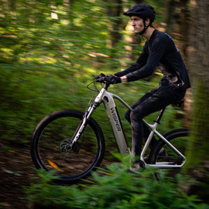 Cyclist riding a Wisper Wayfarer electric bike through a lush forest trail, showcasing its robust off-road capabilities.