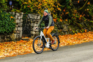 Man riding an electric bike through a scenic autumn setting with vibrant leaves, showcasing the comfort and versatility of e-bikes for everyday commuting.